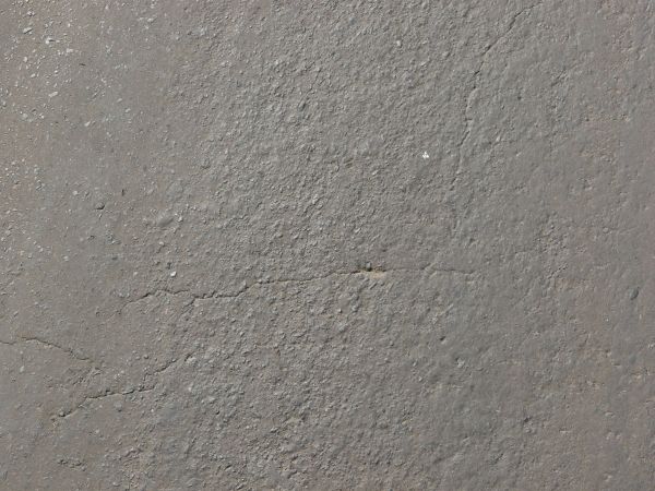 Asphalt texture with a grey surface that is very rough vertically through the center, and slightly smoother on either side. Several cracks run through the surface.
